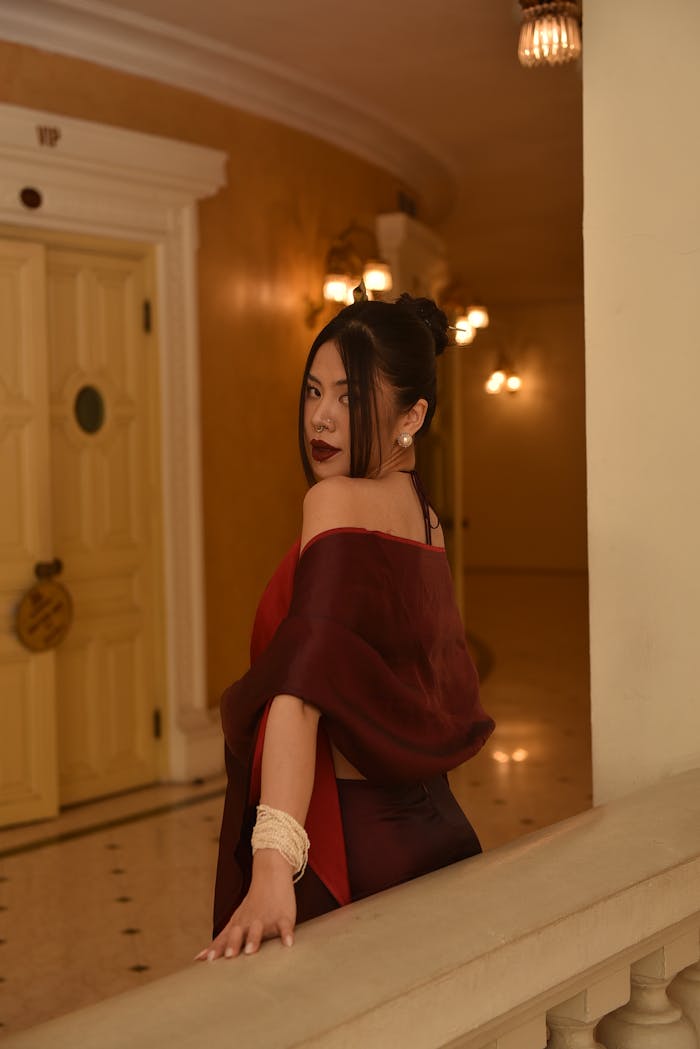 A stylish woman in evening attire poses with elegance in a luxurious hallway.