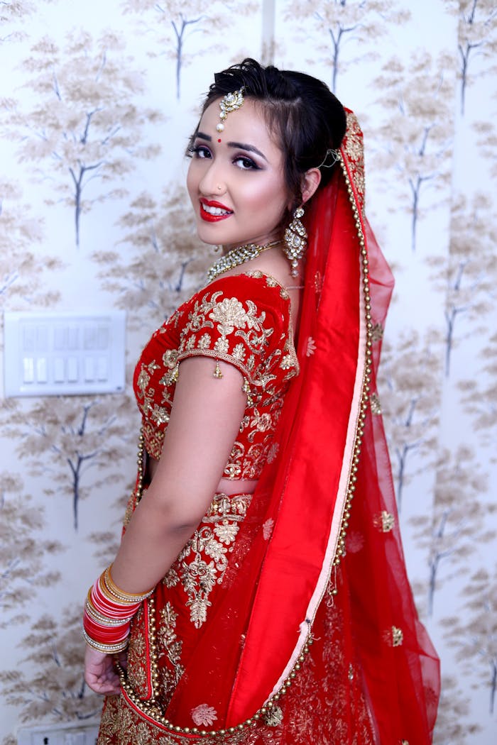 Beautiful South Asian bride in a traditional red saree with intricate gold embroidery.